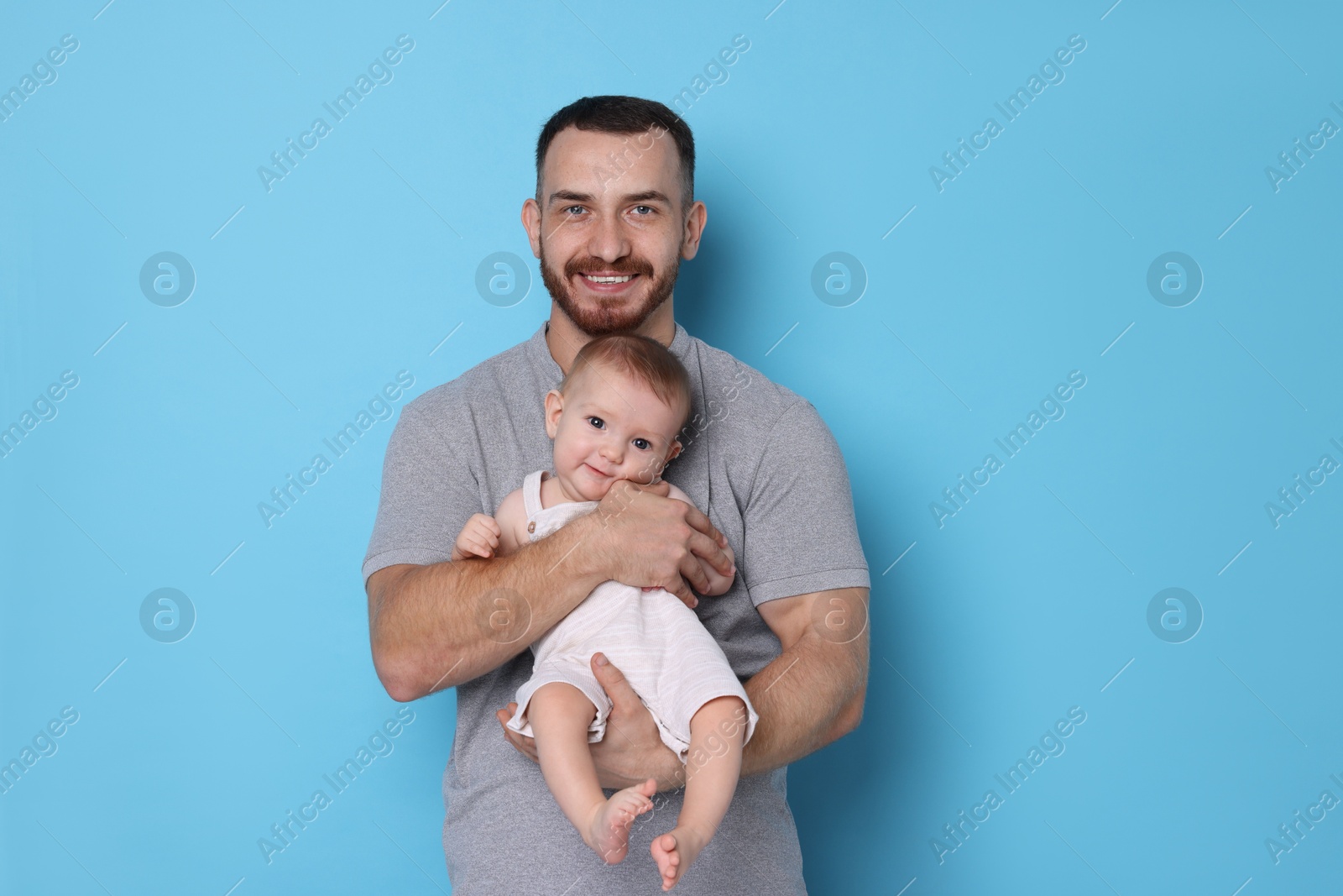 Photo of Father with his cute baby on light blue background