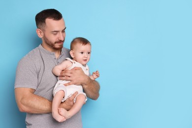 Father with his cute baby on light blue background, space for text