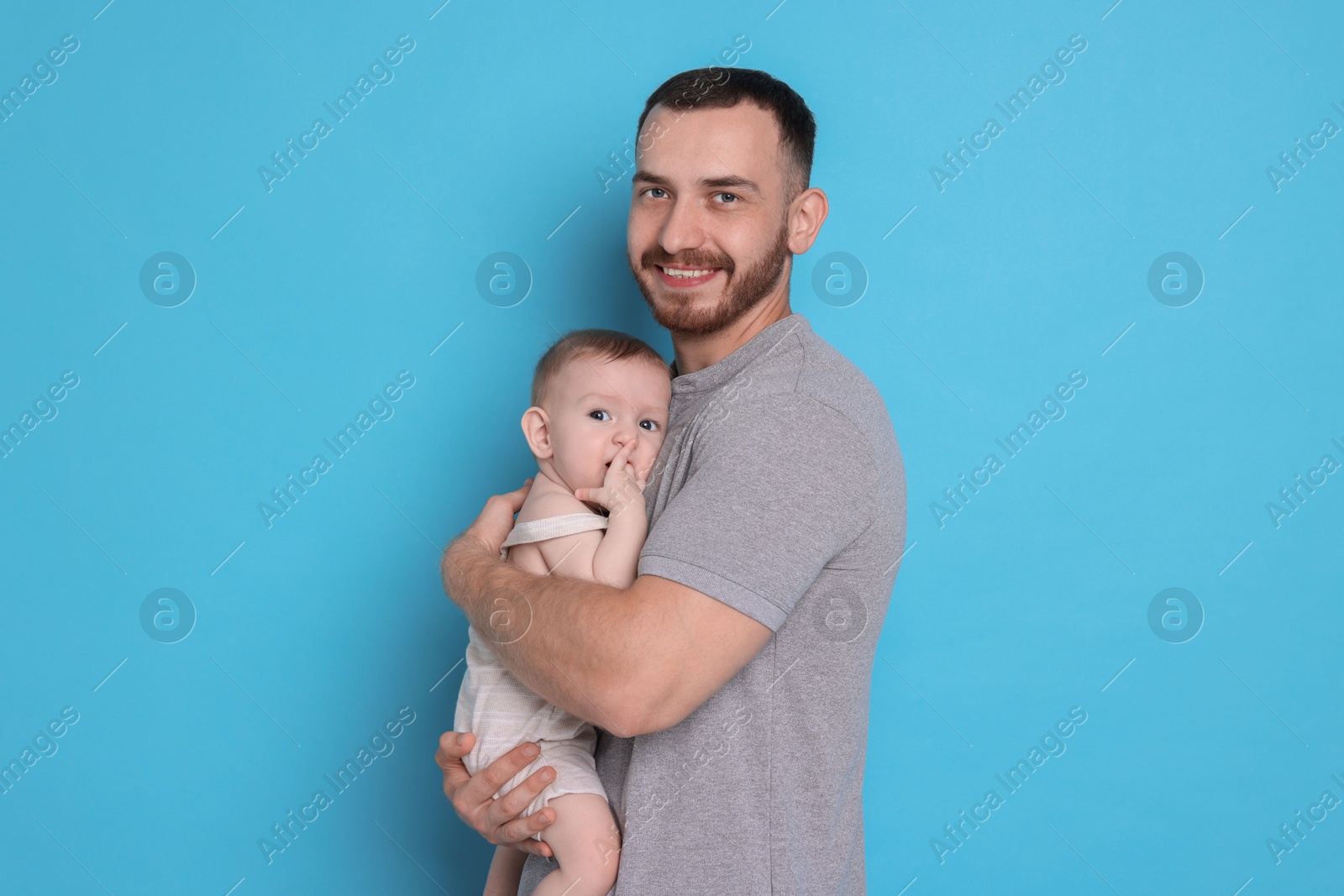 Photo of Father with his cute baby on light blue background