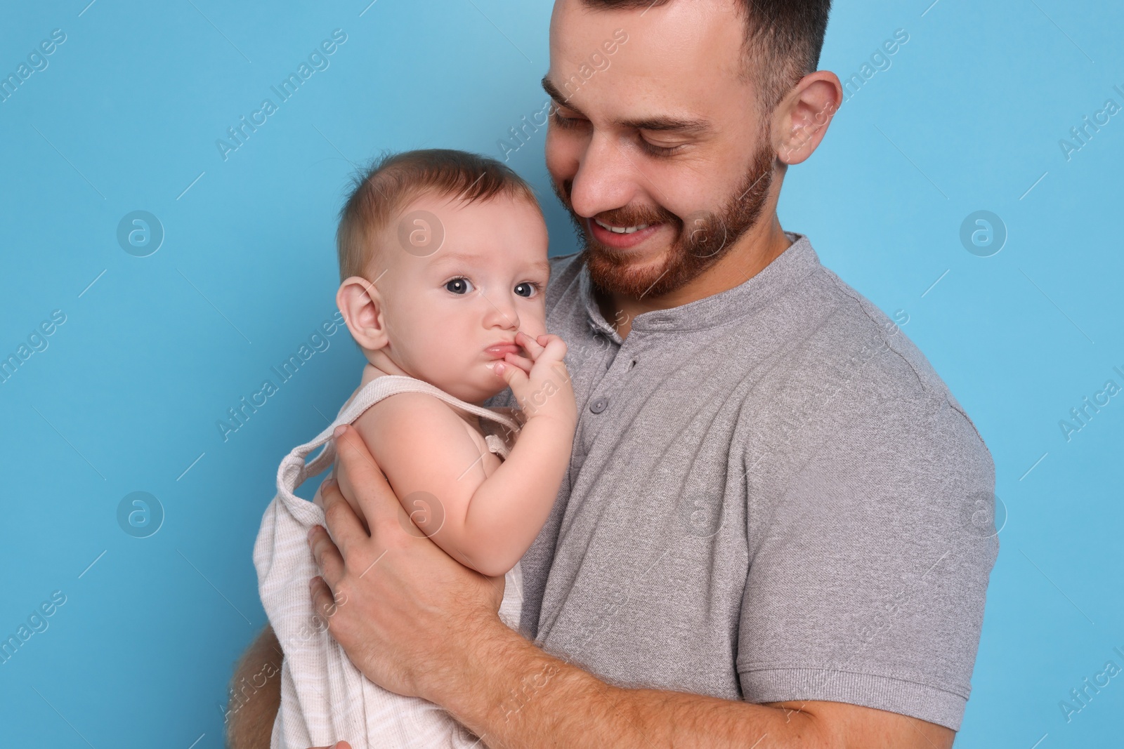 Photo of Father with his cute baby on light blue background