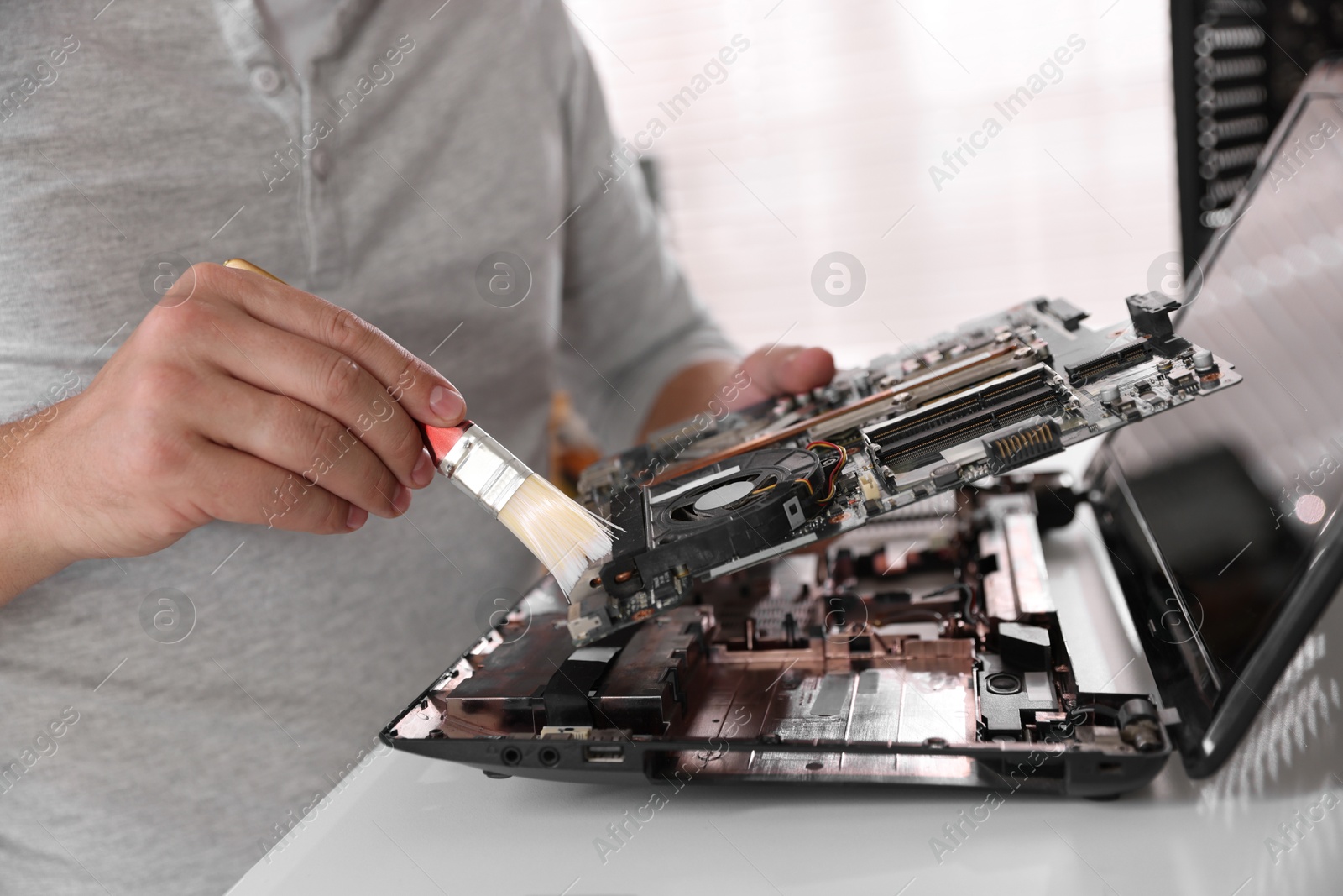 Photo of Man cleaning motherboard with brush at white table, closeup