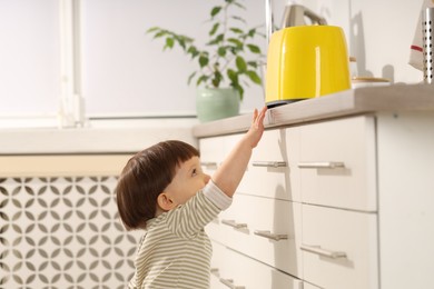 Photo of Little boy playing with toaster in kitchen. Dangerous situation