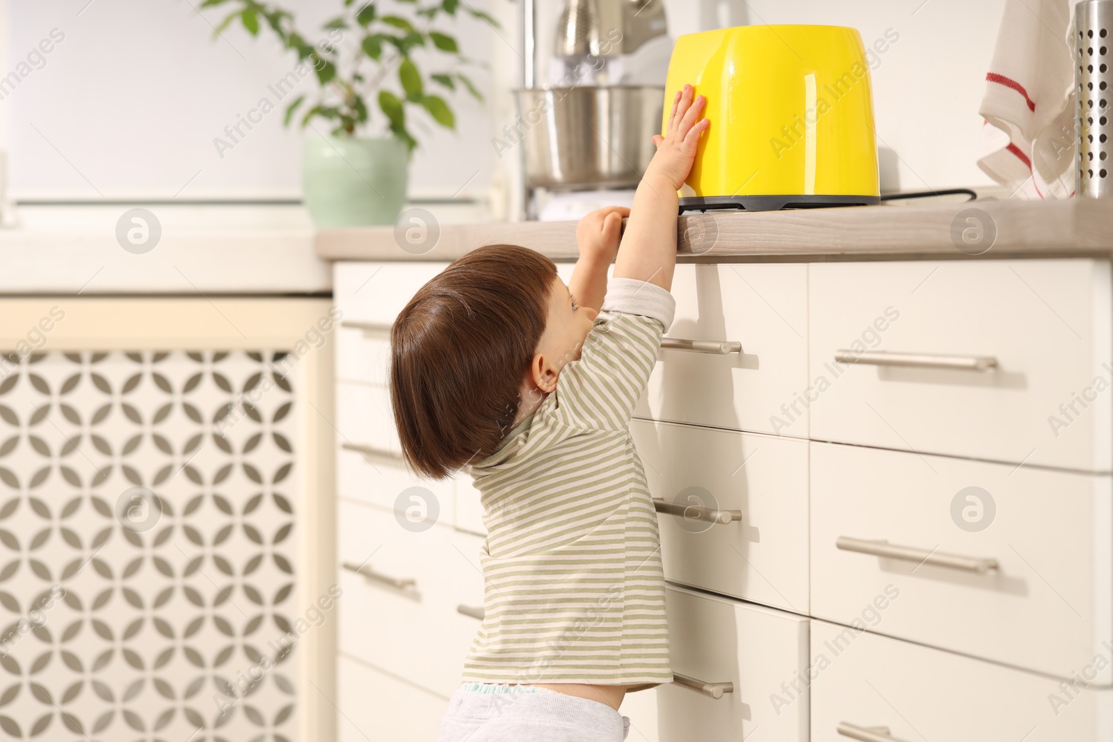 Photo of Little boy playing with toaster in kitchen. Dangerous situation