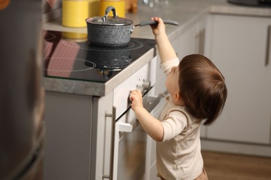 Photo of Little boy playing with pot on stove in kitchen. Dangerous situation