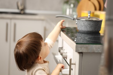 Photo of Little boy playing with pot on stove in kitchen. Dangerous situation