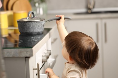 Photo of Little boy playing with pot on stove in kitchen. Dangerous situation