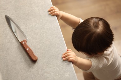 Photo of Little boy reaching towards knife on kitchen counter, above view. Dangerous situation