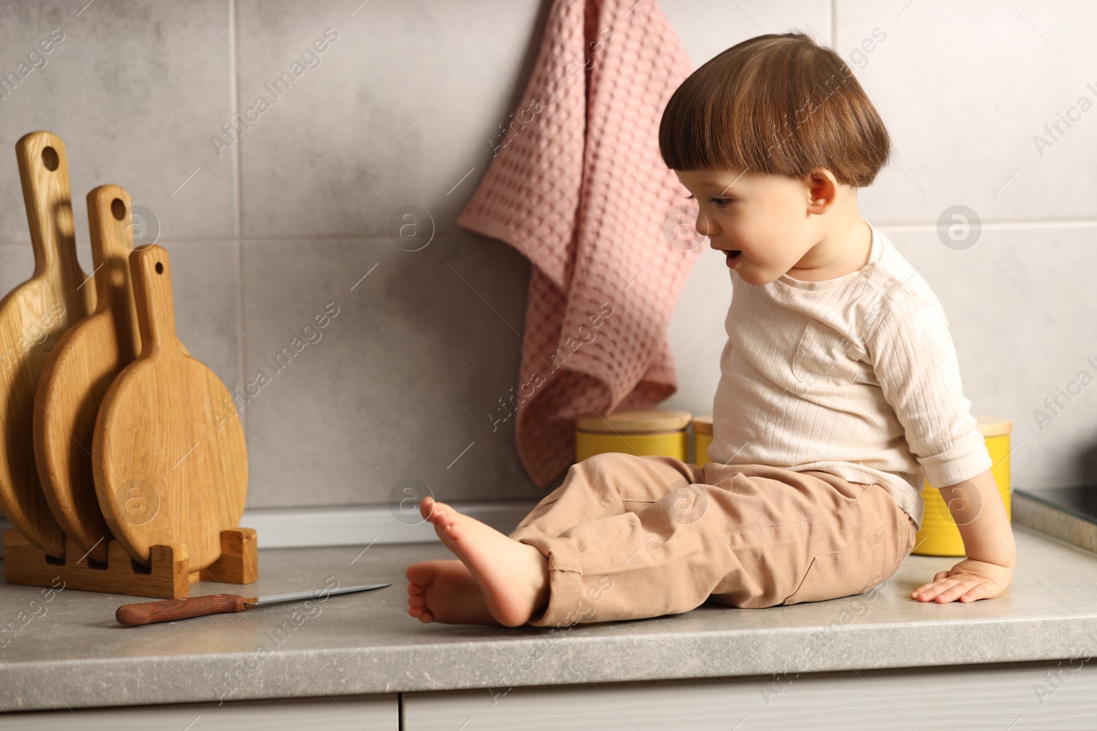 Photo of Little boy near knife on kitchen counter. Dangerous situation