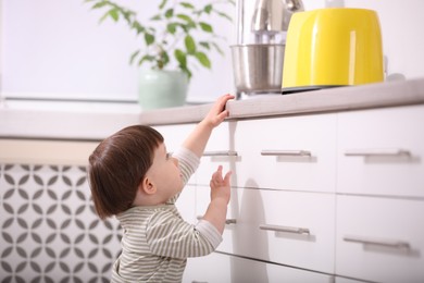 Photo of Little boy playing with toaster in kitchen. Dangerous situation