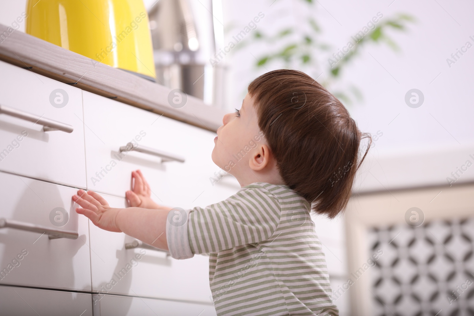 Photo of Little boy near kitchen counter indoors. Dangerous situation