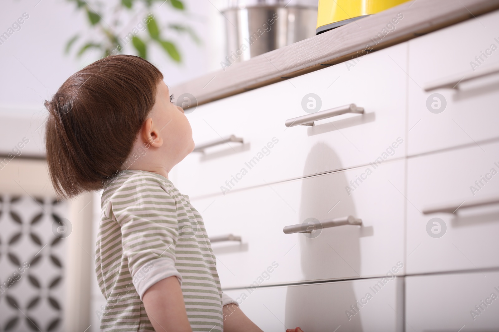 Photo of Little boy near kitchen counter indoors. Dangerous situation