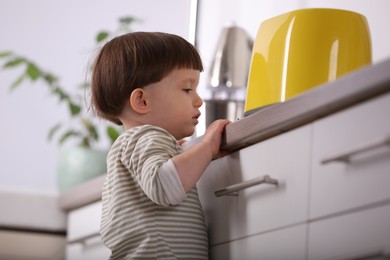 Photo of Little boy playing with toaster in kitchen. Dangerous situation