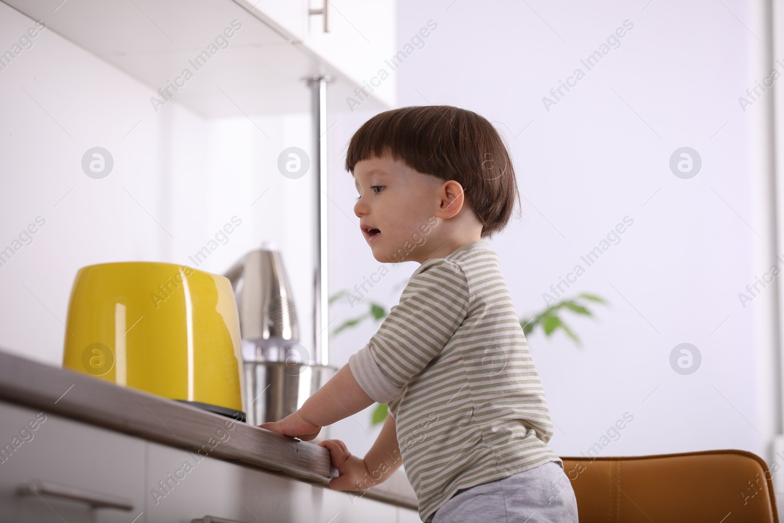 Photo of Little boy playing with toaster in kitchen, low angle view. Dangerous situation