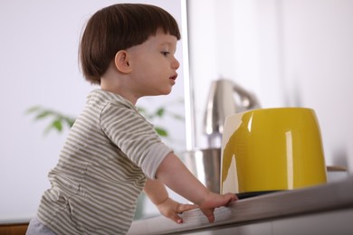 Photo of Little boy playing with toaster in kitchen. Dangerous situation