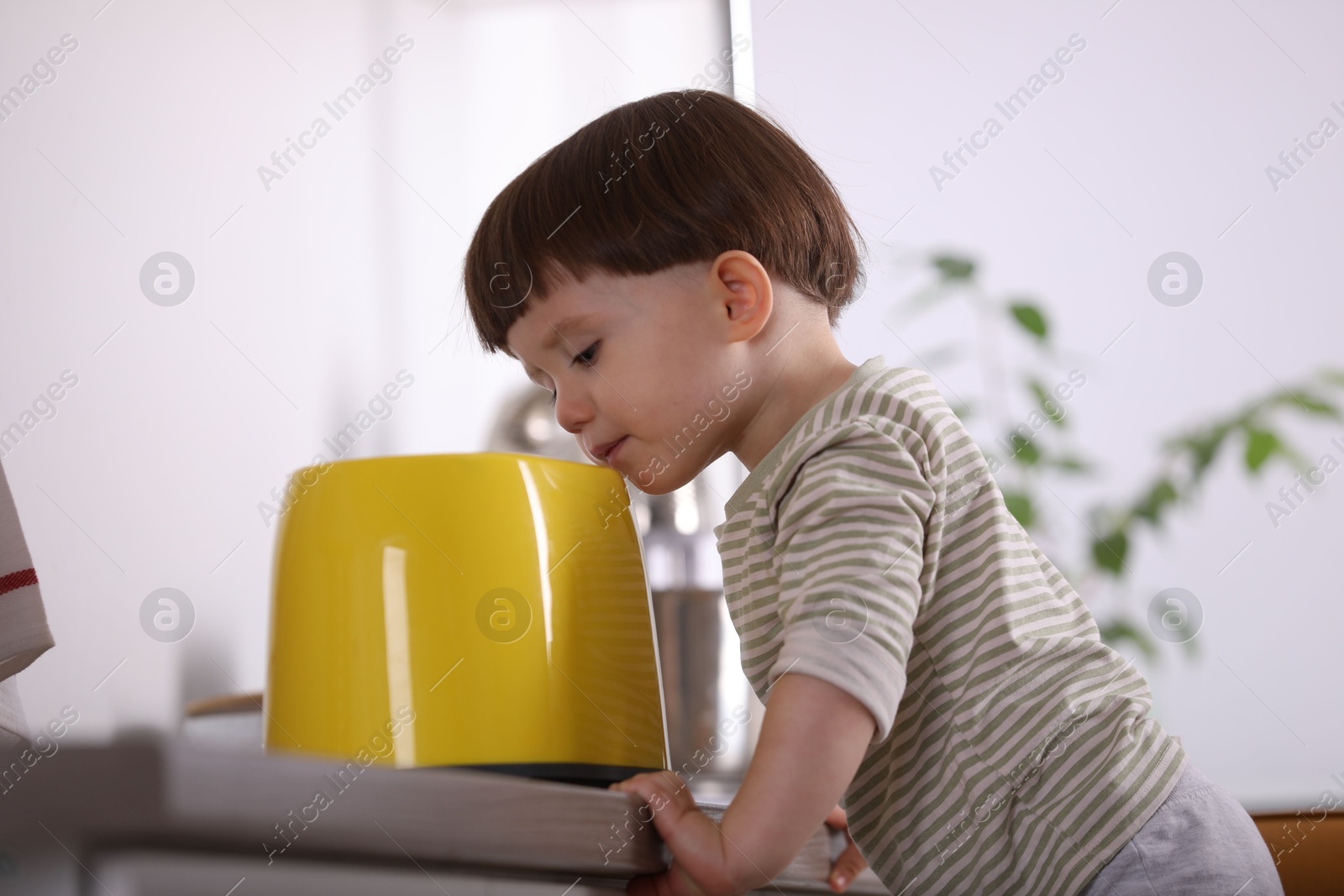 Photo of Little boy playing with toaster in kitchen. Dangerous situation