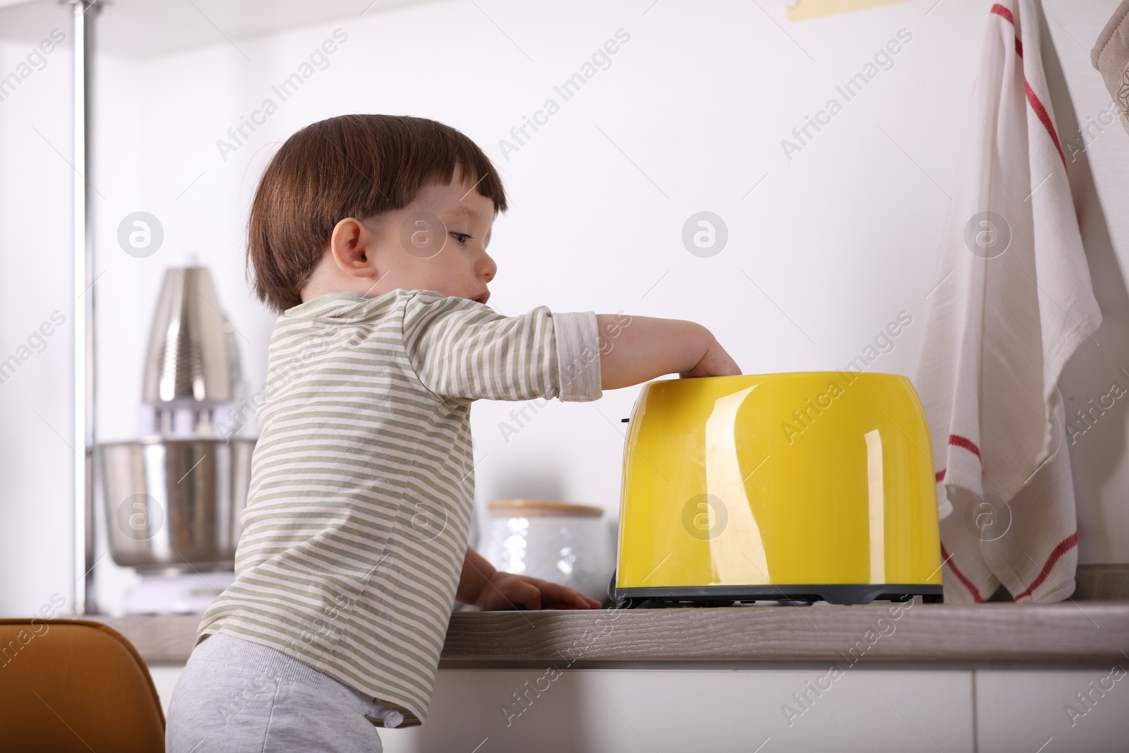 Photo of Little boy playing with toaster in kitchen. Dangerous situation