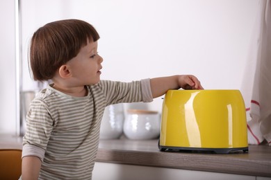 Photo of Little boy playing with toaster in kitchen. Dangerous situation