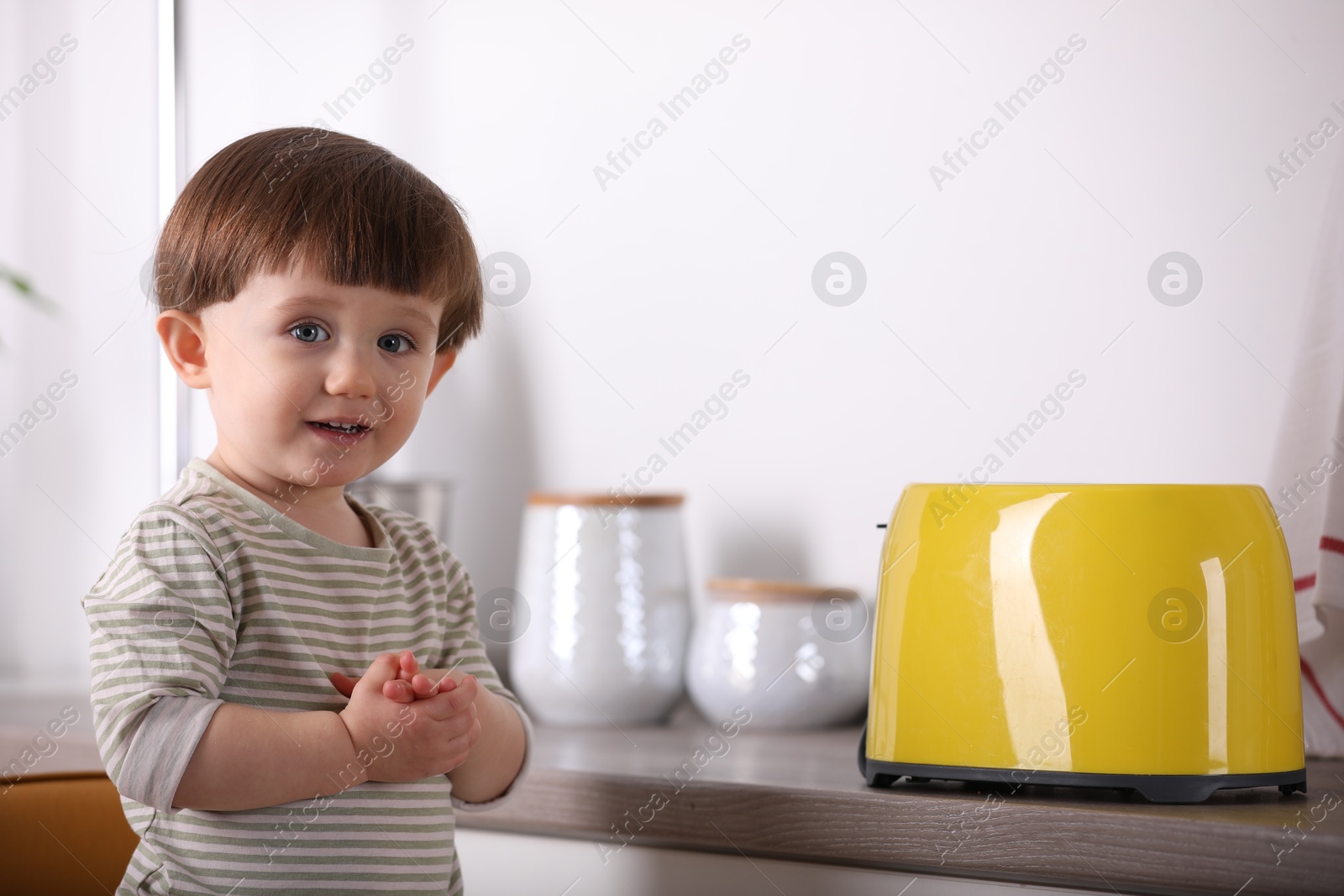 Photo of Little boy playing with toaster in kitchen. Dangerous situation