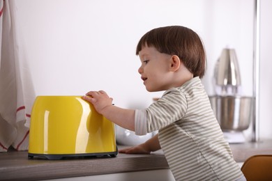 Photo of Little boy playing with toaster in kitchen. Dangerous situation