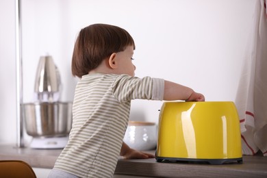 Photo of Little boy playing with toaster in kitchen. Dangerous situation