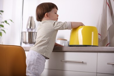 Photo of Little boy playing with toaster in kitchen. Dangerous situation