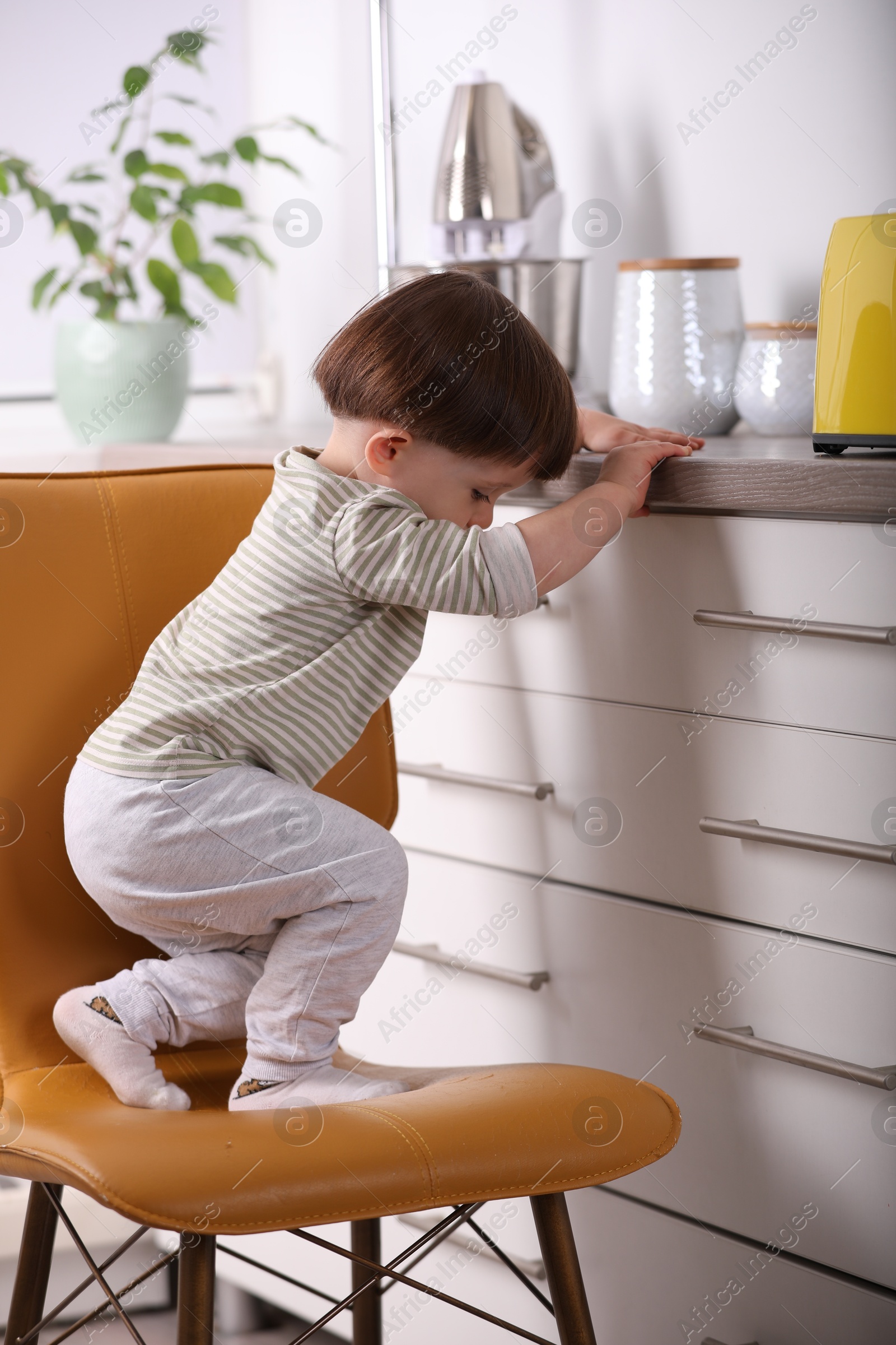 Photo of Little boy playing on chair in kitchen. Dangerous situation