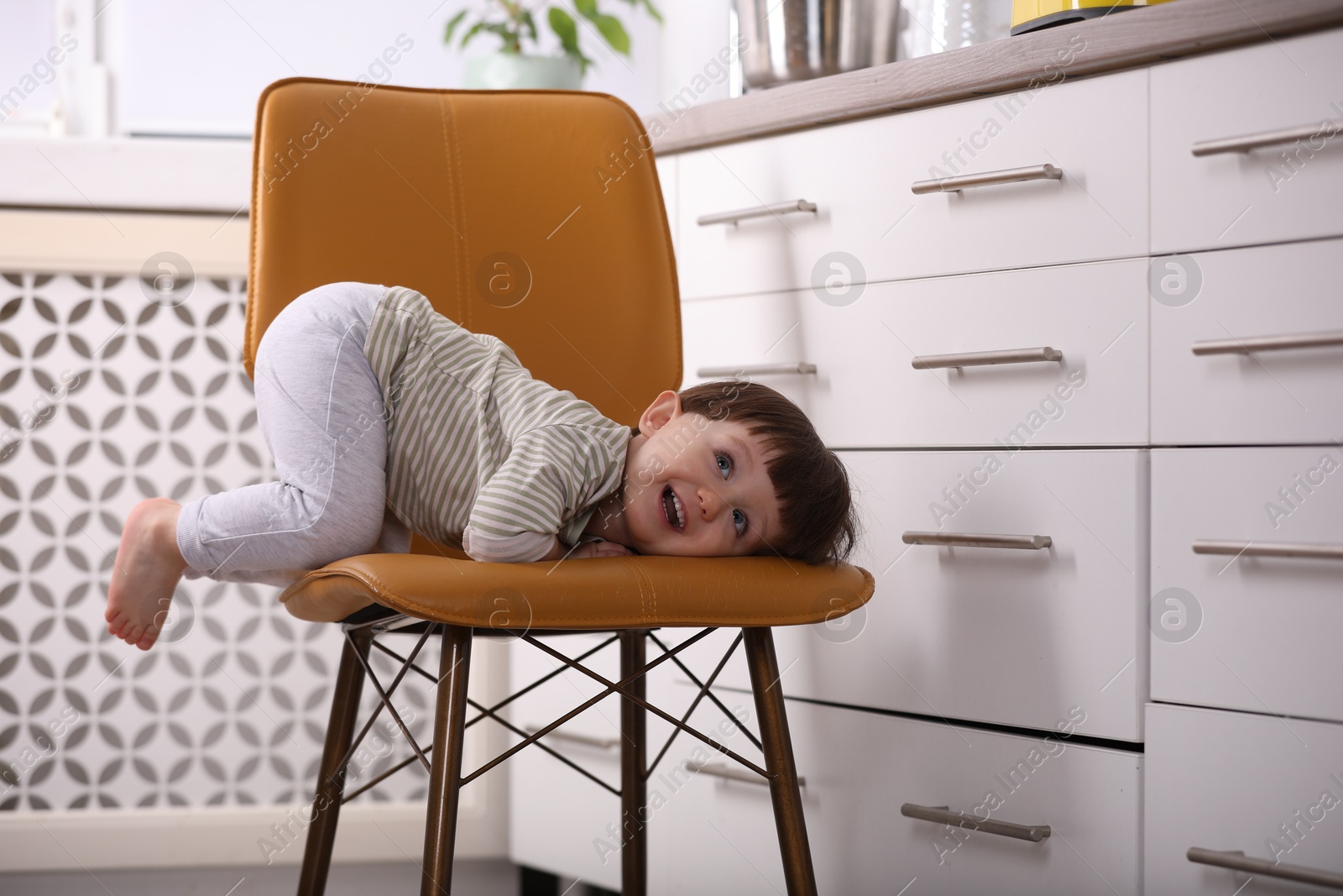 Photo of Little boy playing on chair in kitchen. Dangerous situation