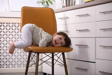 Photo of Little boy playing on chair in kitchen. Dangerous situation