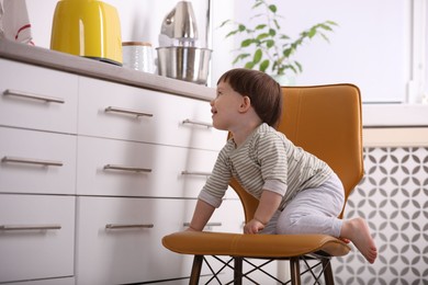 Photo of Little boy playing on chair in kitchen. Dangerous situation