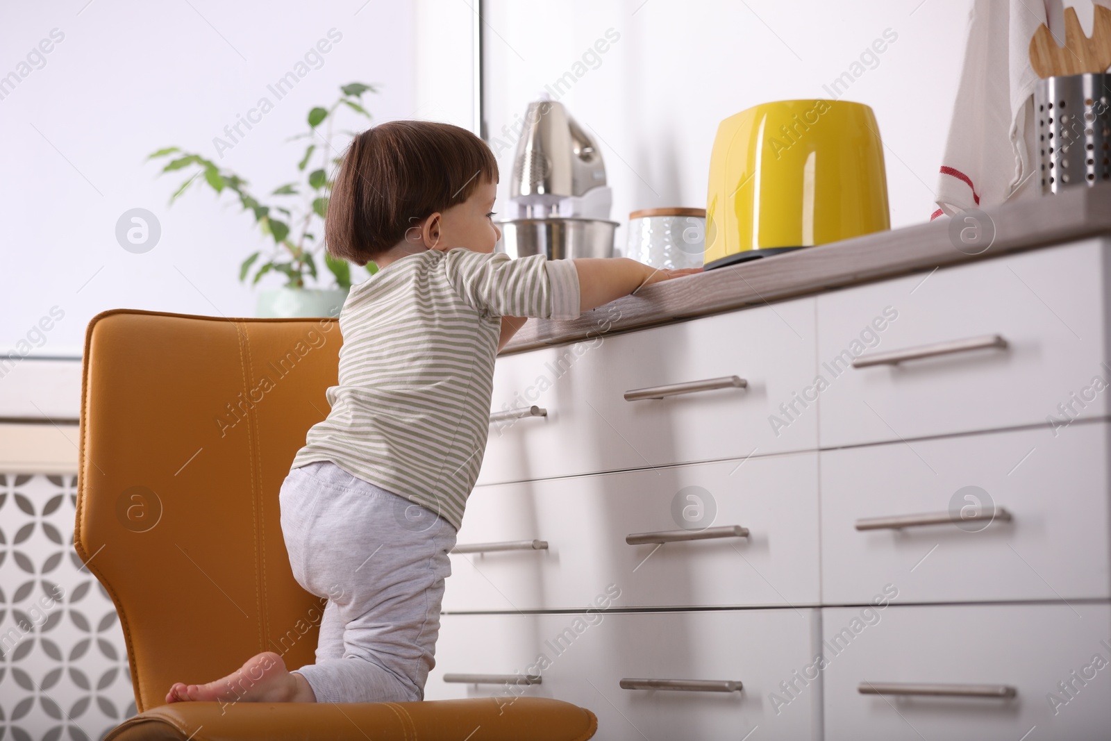 Photo of Little boy playing with toaster in kitchen. Dangerous situation