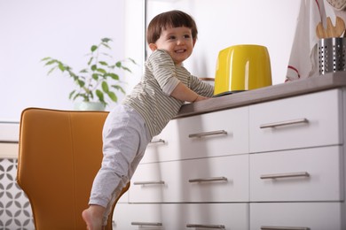 Photo of Little boy playing with toaster in kitchen. Dangerous situation