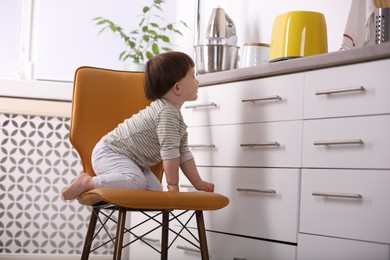 Photo of Little boy playing on chair in kitchen. Dangerous situation