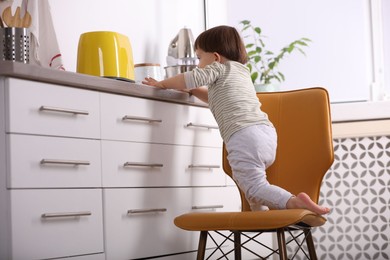 Photo of Little boy playing with toaster in kitchen. Dangerous situation