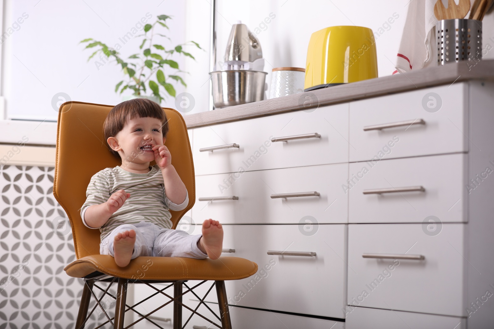 Photo of Little boy playing on chair in kitchen. Dangerous situation