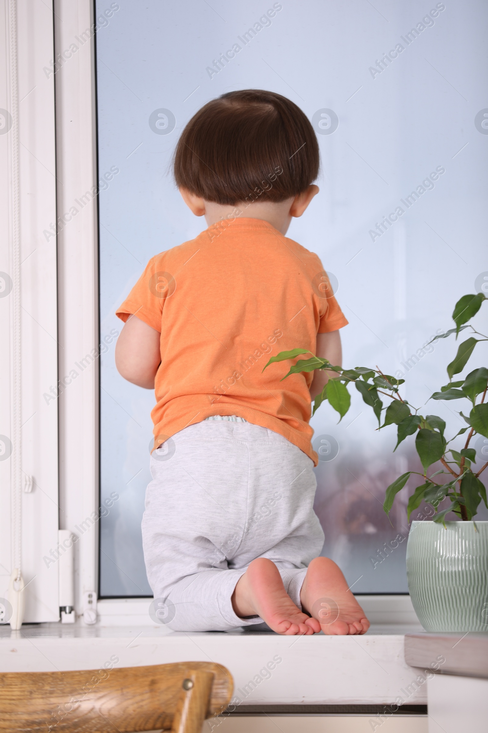 Photo of Little boy near window on windowsill, back view. Dangerous situation