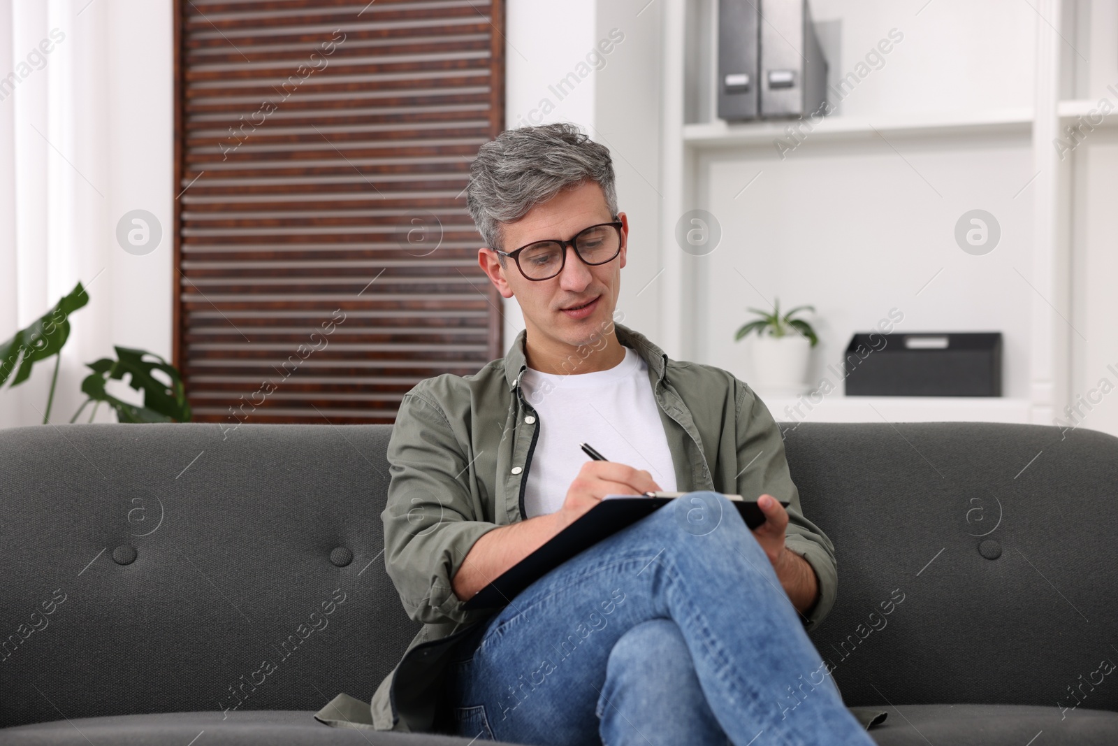 Photo of Professional psychologist with clipboard on sofa in office