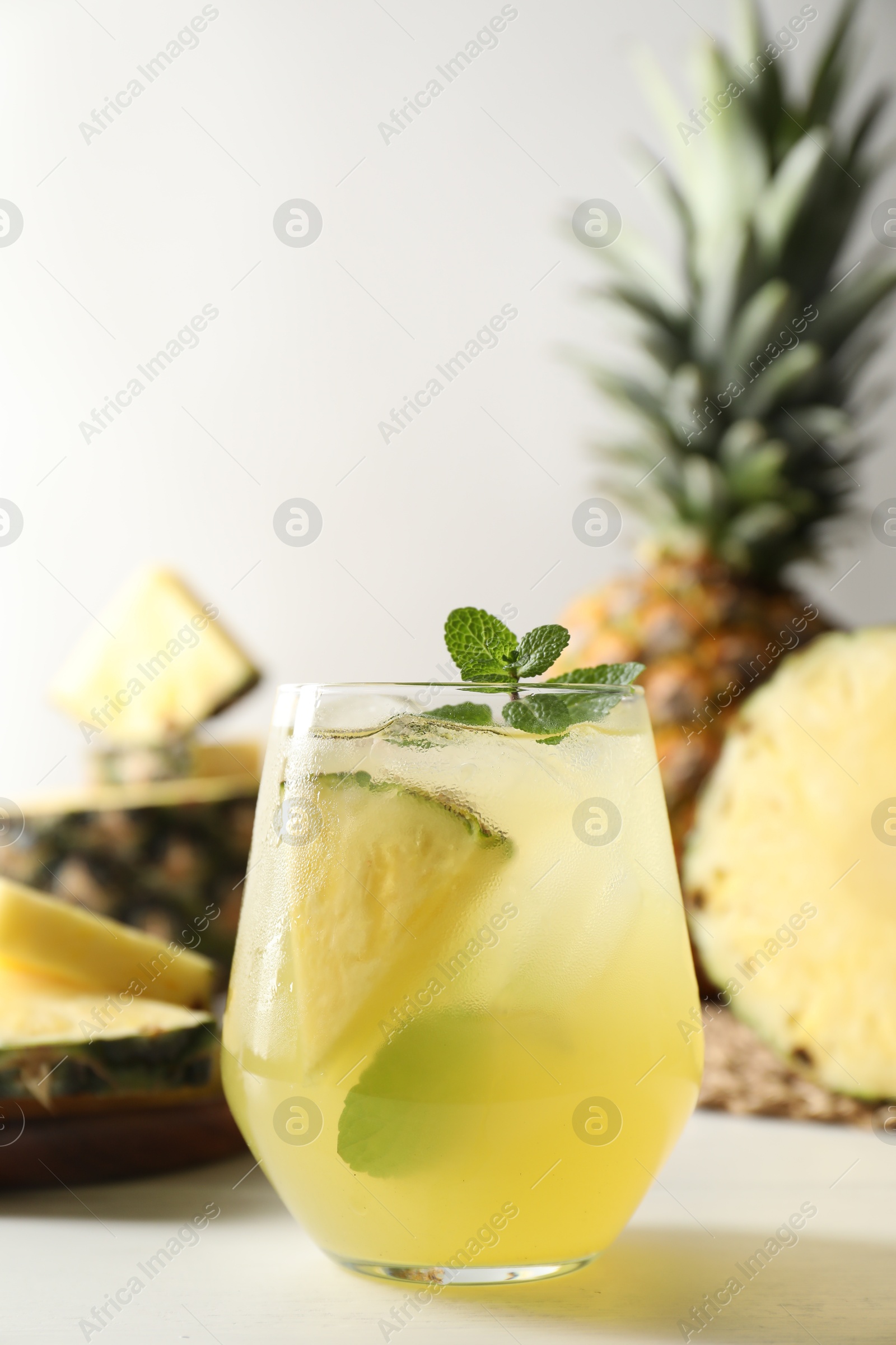 Photo of Tasty pineapple cocktail with mint in glass on light table