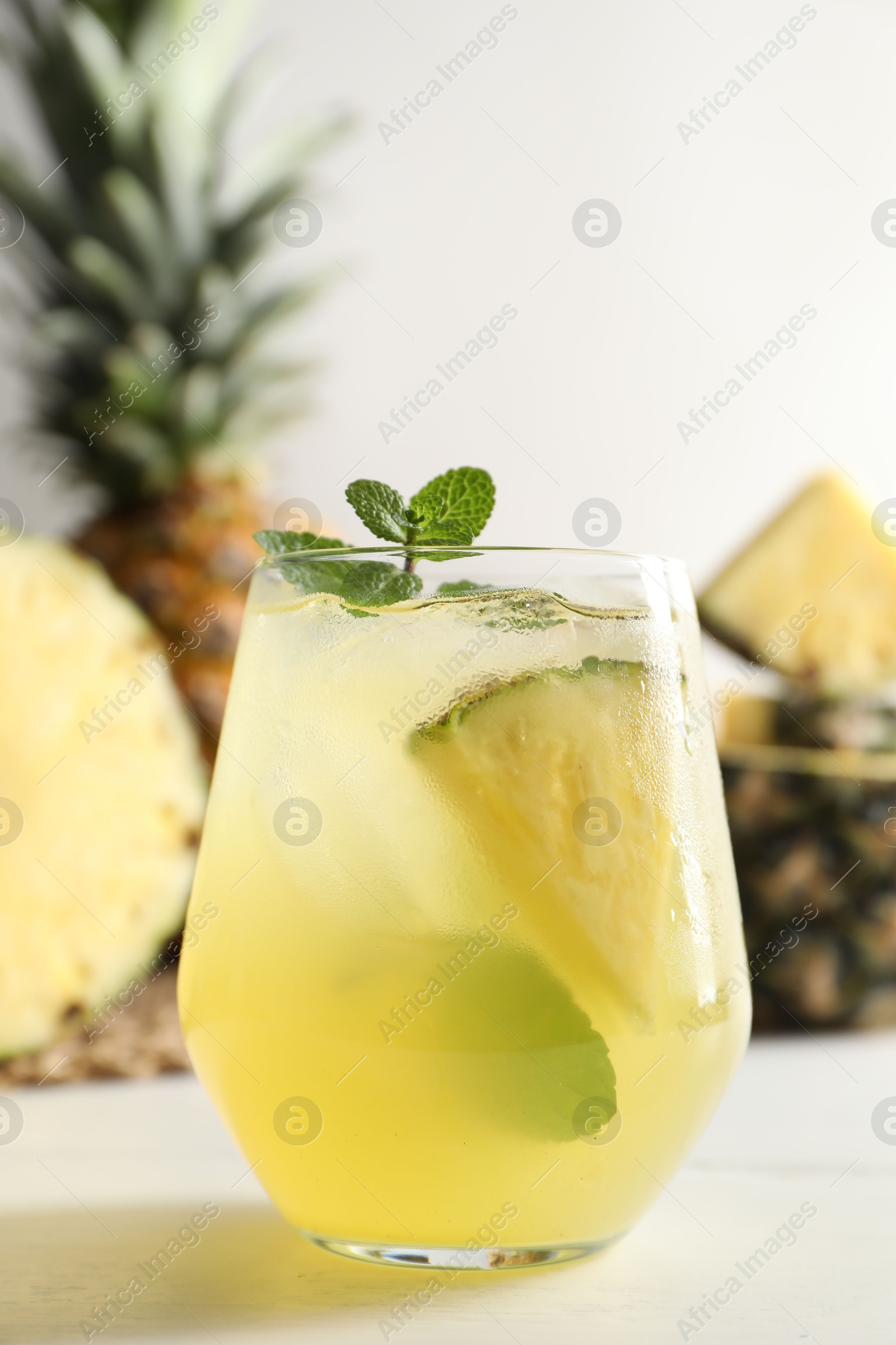 Photo of Tasty pineapple cocktail with mint in glass on light table