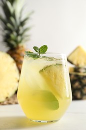 Photo of Tasty pineapple cocktail with mint in glass on light table