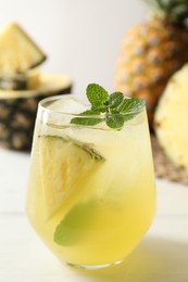 Photo of Tasty pineapple cocktail with mint in glass on light table, closeup