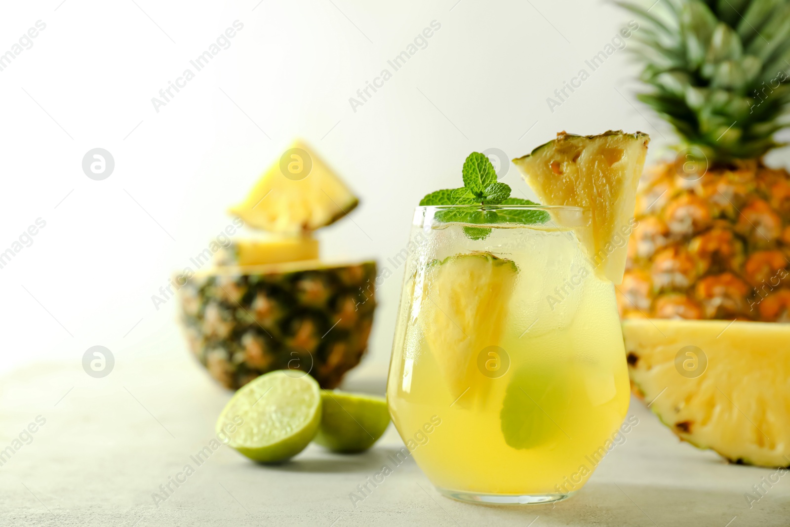 Photo of Tasty pineapple cocktail with mint in glass on light table