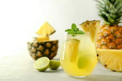 Photo of Tasty pineapple cocktail with mint in glass on light table