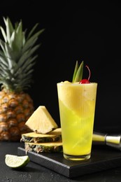 Photo of Tasty pineapple cocktail with cherry in glass on dark table against black background