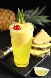 Photo of Tasty pineapple cocktail with cherry in glass on black table, closeup