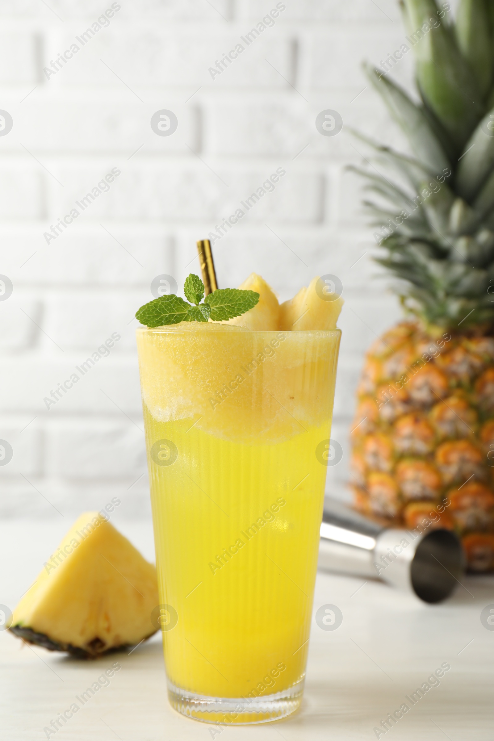 Photo of Tasty pineapple cocktail with mint in glass on light table against white brick wall