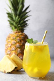 Photo of Tasty pineapple cocktail with mint in glass on gray table