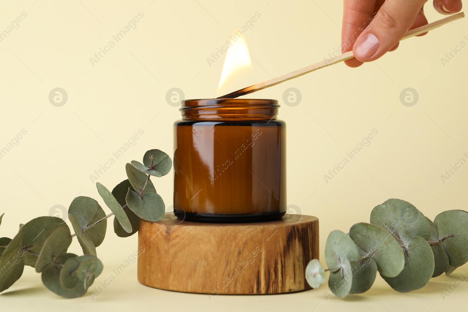 Photo of Woman lighting candle on pale yellow background, closeup