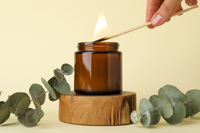 Photo of Woman lighting candle on pale yellow background, closeup