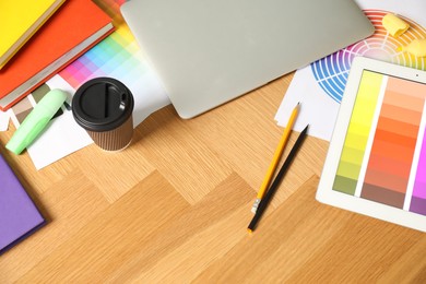 Photo of Designer's workplace with laptop, tablet, palettes and stationery on wooden table, above view