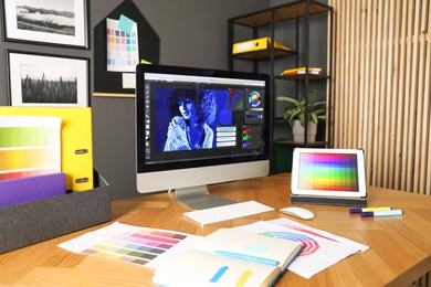 Photo of Designer's workplace with computer, tablet, stationery and palettes on wooden table indoors